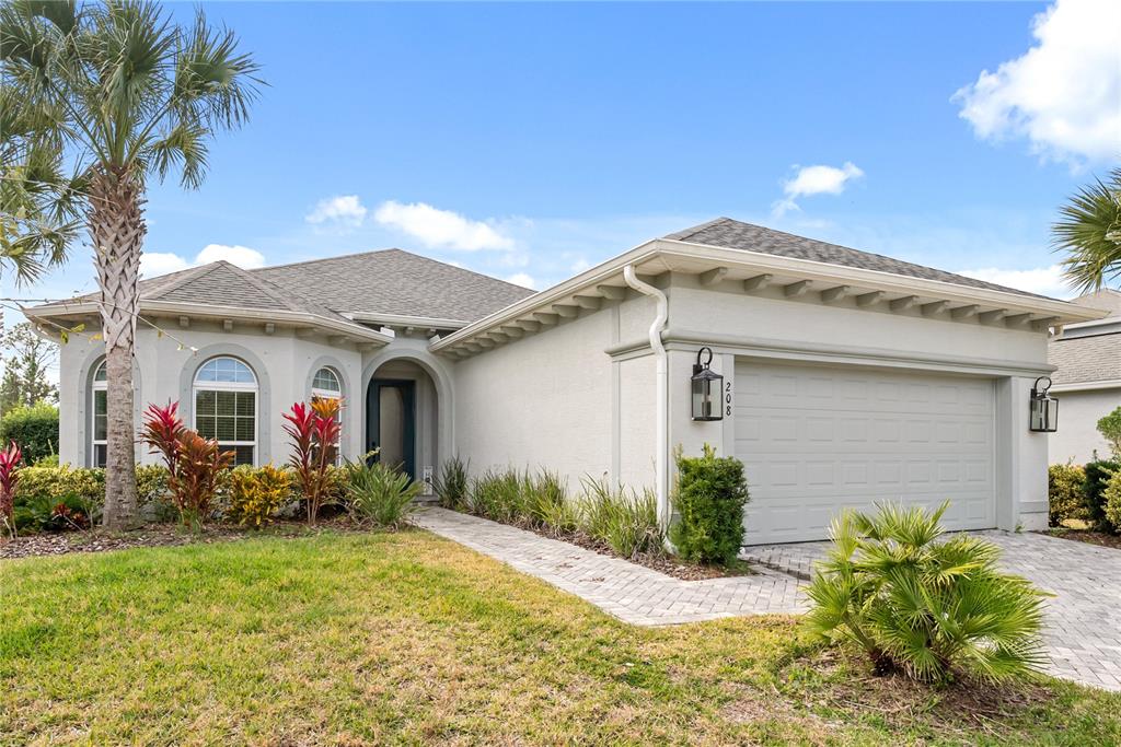 A single-story house with a light-colored stucco exterior, a two-car garage, and palm trees — 208 HERON DRIVE, PALM COAST, FL
