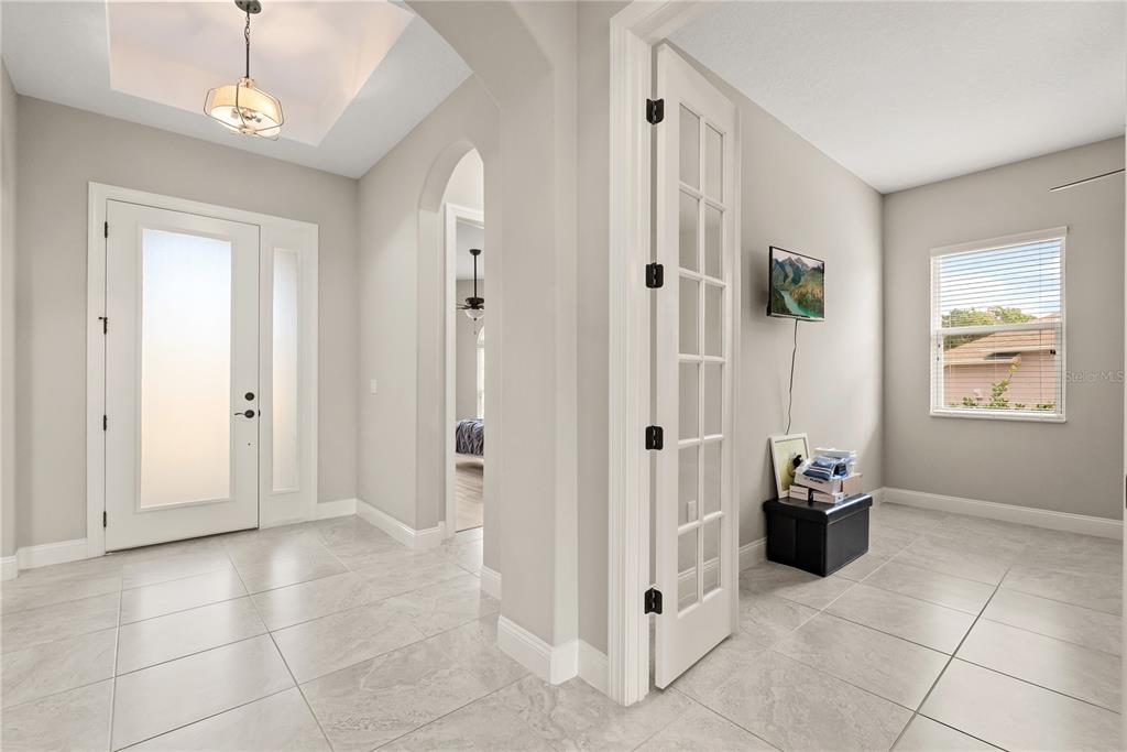 A bright entryway with tile flooring leads to a French door office and arched hallway — 208 HERON DRIVE, PALM COAST, FL