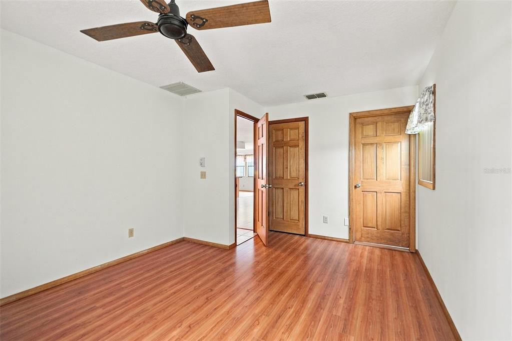 An empty room features wood-look laminate flooring, white walls, a ceiling fan, and two doors — 2151 MEREDITH DRIVE, SPRING HILL, FL