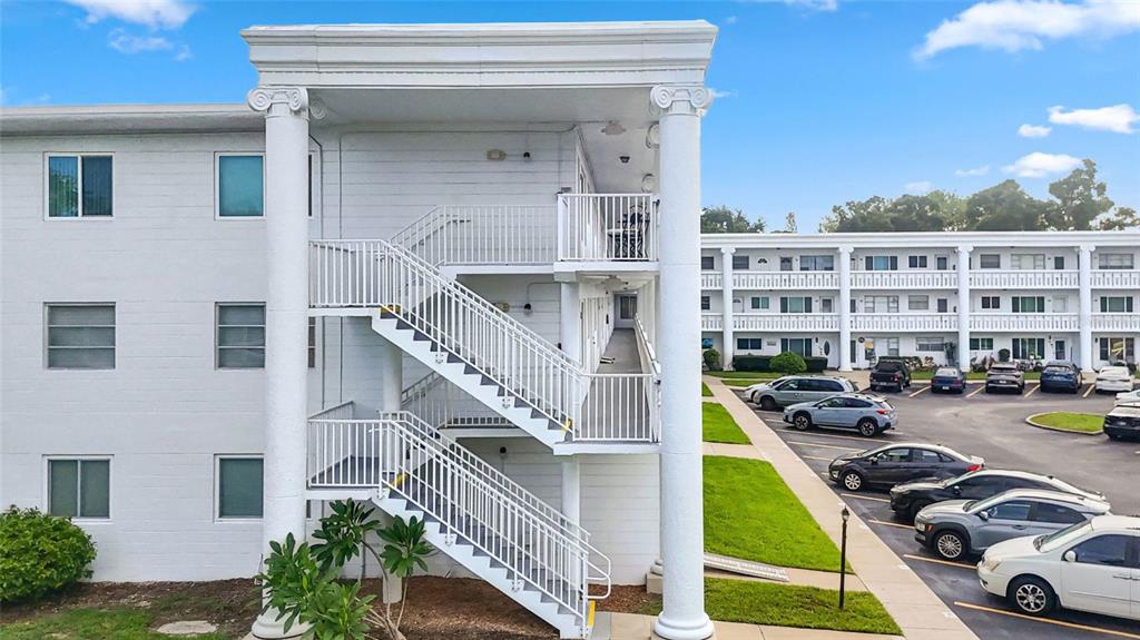 An exterior view of a white apartment building featuring an open-air staircase and parking lot — 2454 AUSTRALIA WAY E UNIT 32, CLEARWATER, FL