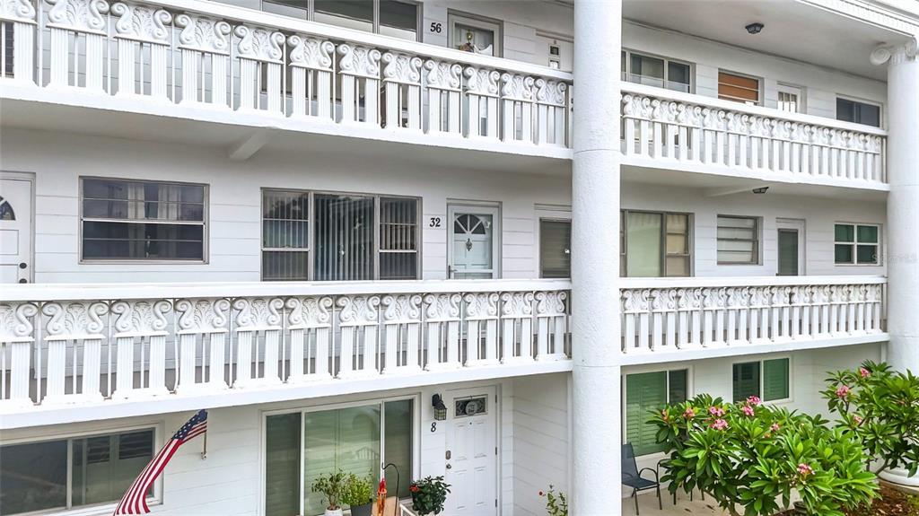 A multi-story apartment building exterior features white balconies with decorative railings and numbered unit doors — 2454 AUSTRALIA WAY E UNIT 32, CLEARWATER, FL