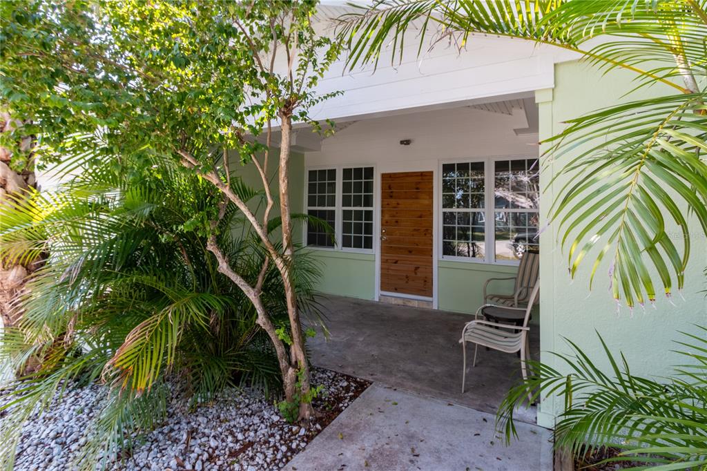 A covered porch with a wooden front door, two chairs, and surrounding palm trees — 750 BAY ESPLANADE, CLEARWATER BEACH, FL