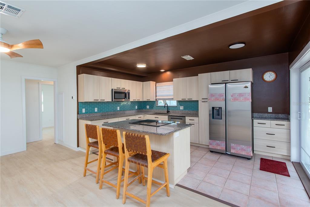 A kitchen features light wood cabinets, a granite island with bar stools, and teal backsplash tiles — 750 BAY ESPLANADE, CLEARWATER BEACH, FL