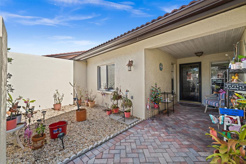 A paved courtyard entrance features a gravel garden bed with potted plants and a porch — 3709 MIGUEL WAY UNIT 8602, SARASOTA, FL