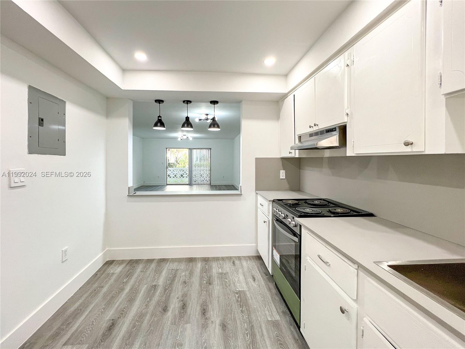 A kitchen with white cabinets, gray countertops, and wood-look flooring overlooks an adjacent living area — 2005 Sans Souci Blvd # 107, North Miami FL 33181, NORTH MIAMI, FL