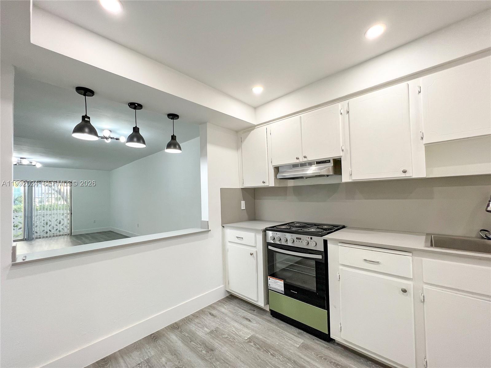 A kitchen features white cabinets, stainless steel appliances, and a pass-through window to the living area — 2005 Sans Souci Blvd # 107, North Miami FL 33181, NORTH MIAMI, FL
