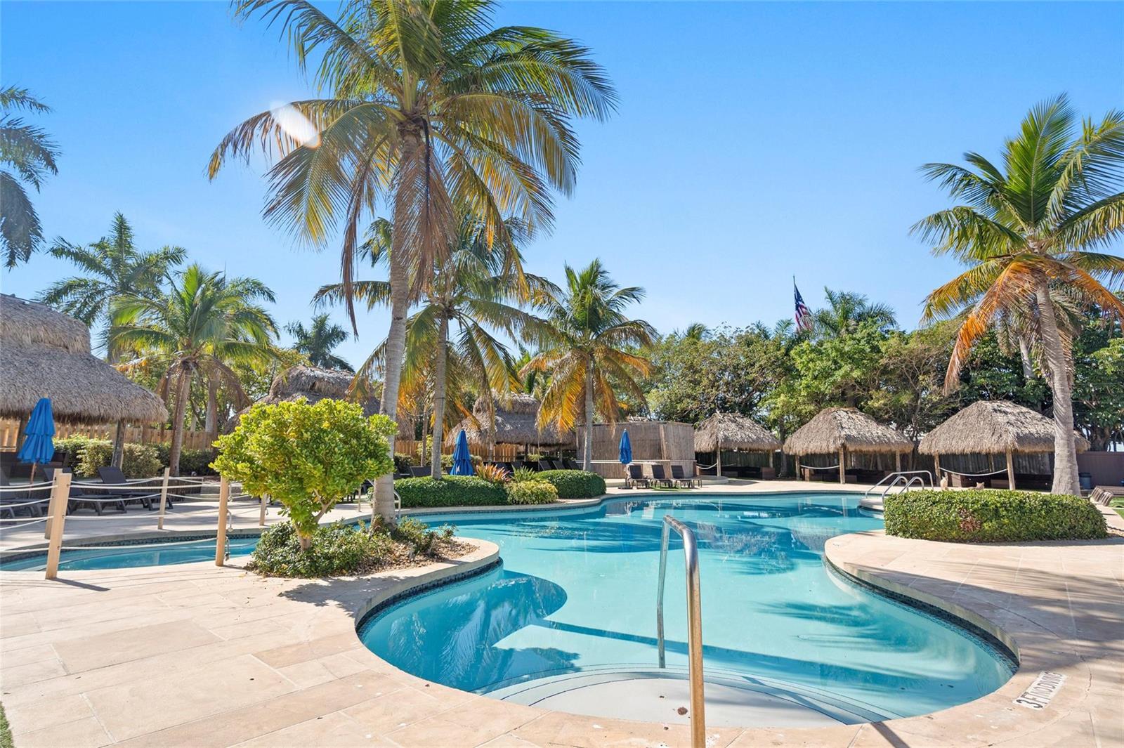 A tropical swimming pool area features palm trees, thatched-roof cabanas, and paved lounge decking — 104000 Overseas Highway, Key Largo FL 33037, KEY LARGO, FL