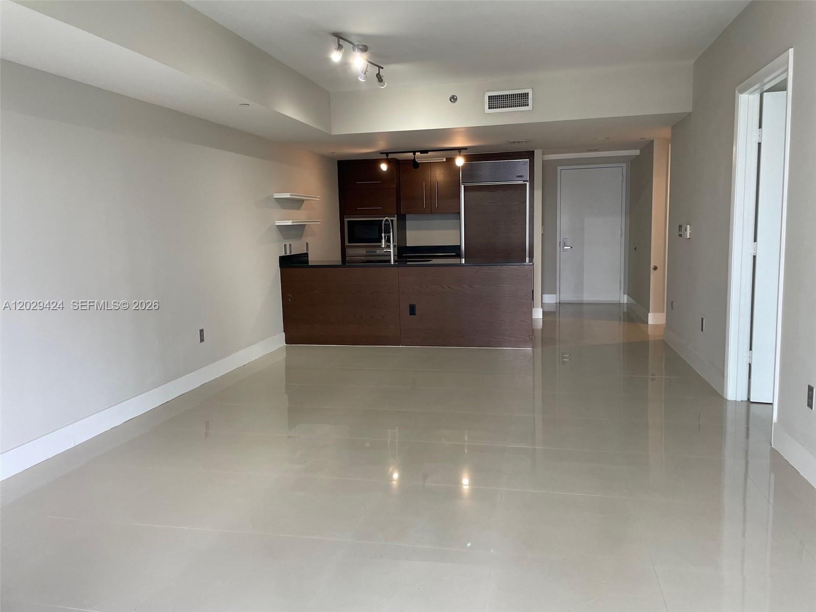 An open-concept kitchen with dark wood cabinetry and a breakfast bar overlooks a tiled living area — 475 Brickell Ave # 414, Miami FL 33131, MIAMI, FL