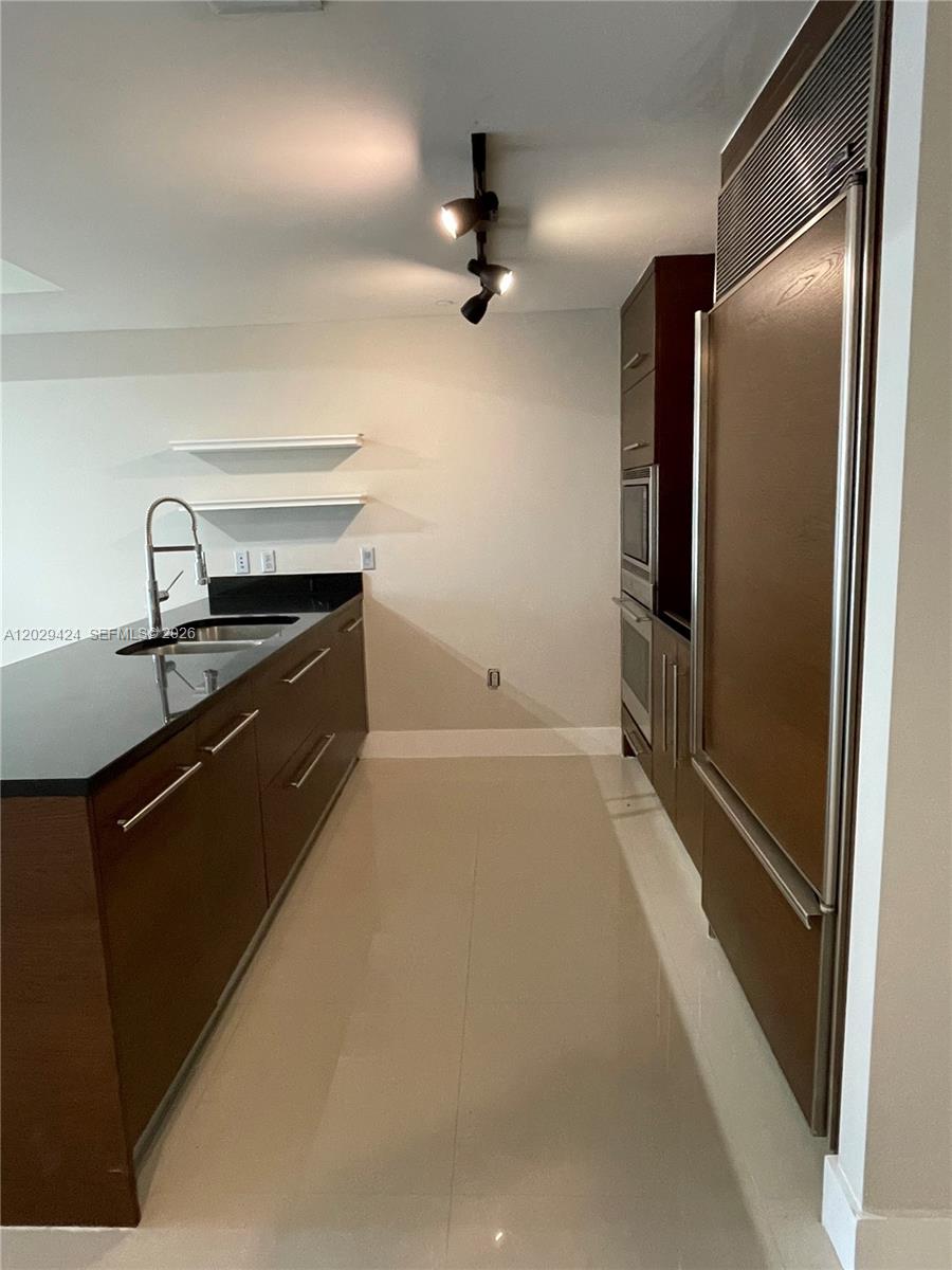 A modern kitchen features dark wood cabinetry, black countertops, stainless steel appliances, and tile flooring — 475 Brickell Ave # 414, Miami FL 33131, MIAMI, FL