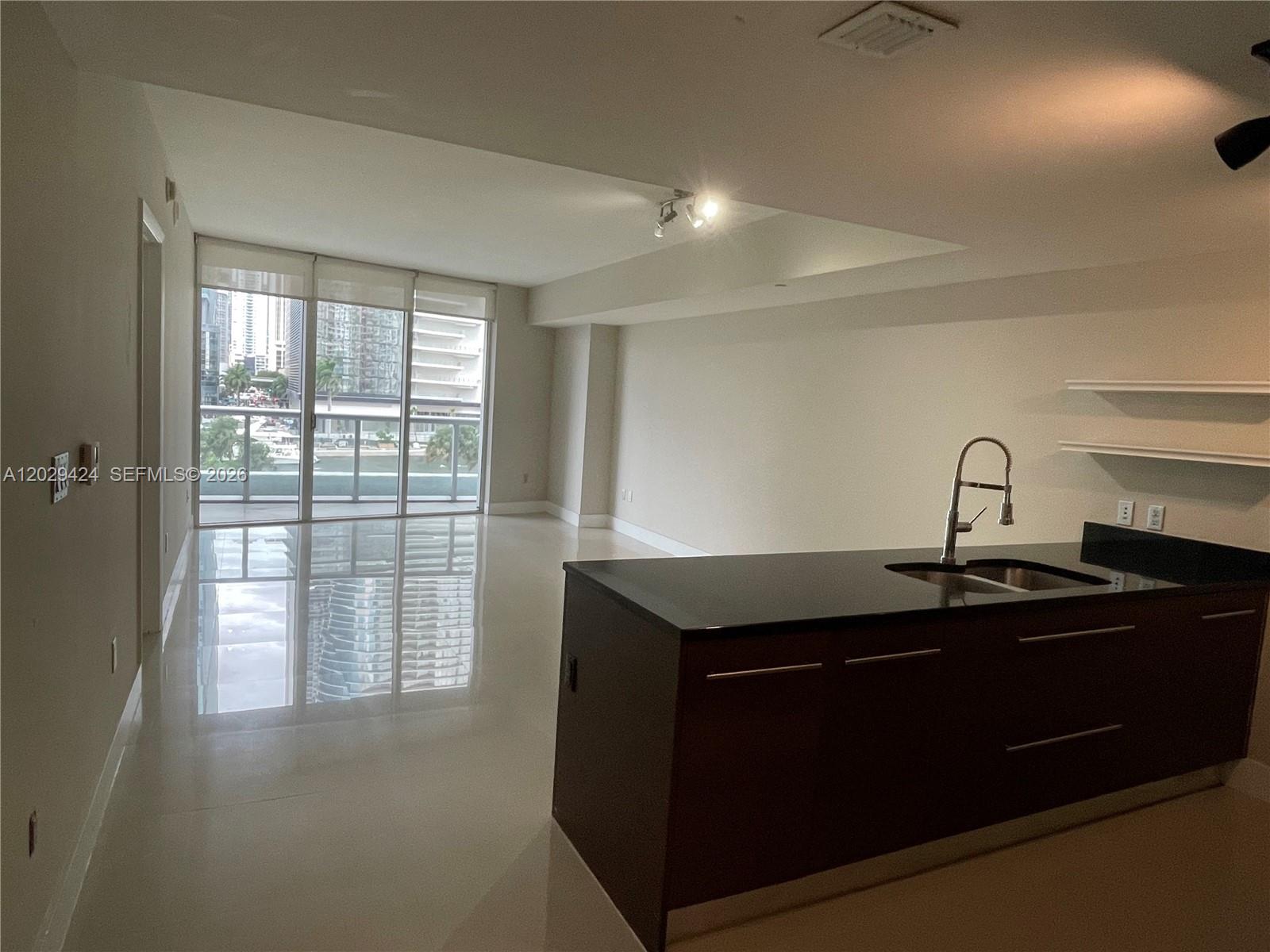 A modern kitchen island with a dark countertop faces a bright, open-concept living area — 475 Brickell Ave # 414, Miami FL 33131, MIAMI, FL