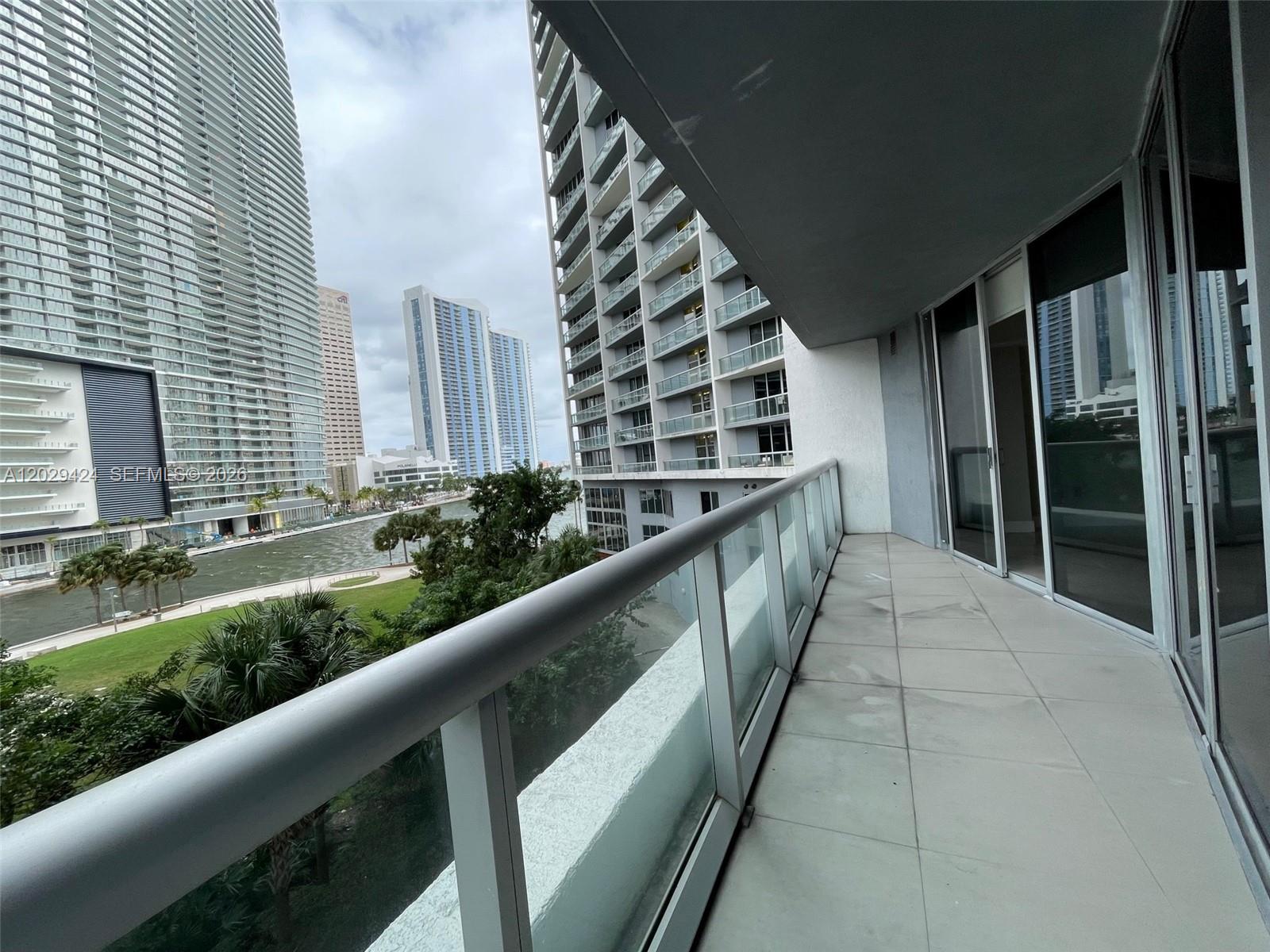 A balcony with a glass railing overlooks a river, park, and surrounding high-rise buildings — 475 Brickell Ave # 414, Miami FL 33131, MIAMI, FL