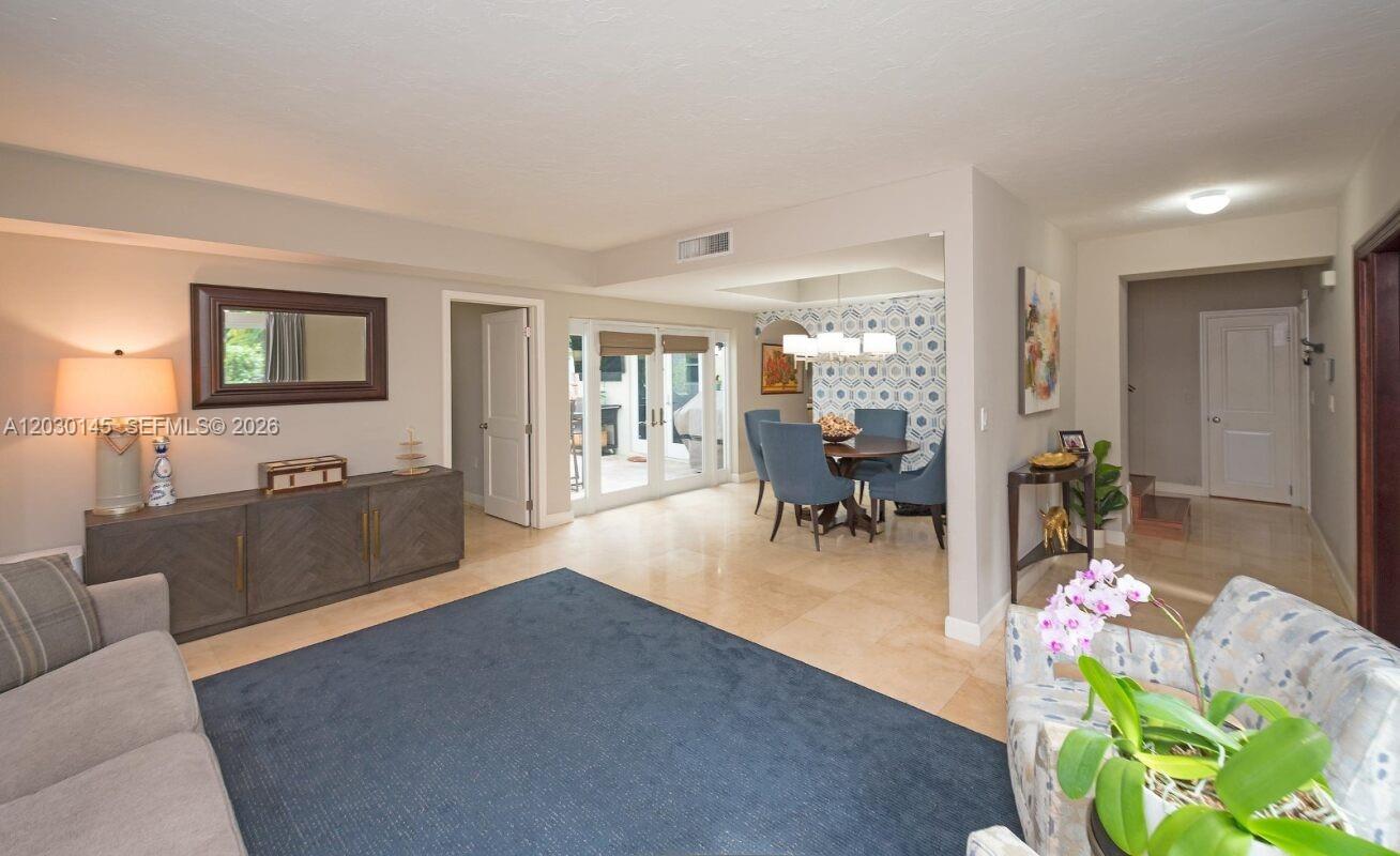 A living room with a blue rug, dining area, and tile flooring leads to patio doors — 423 Alhambra Cir, Coral Gables FL 33134, CORAL GABLES, FL