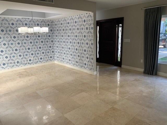 An empty room with beige tile flooring, a geometric patterned accent wall, and a chandelier — 423 Alhambra Cir, Coral Gables FL 33134, CORAL GABLES, FL