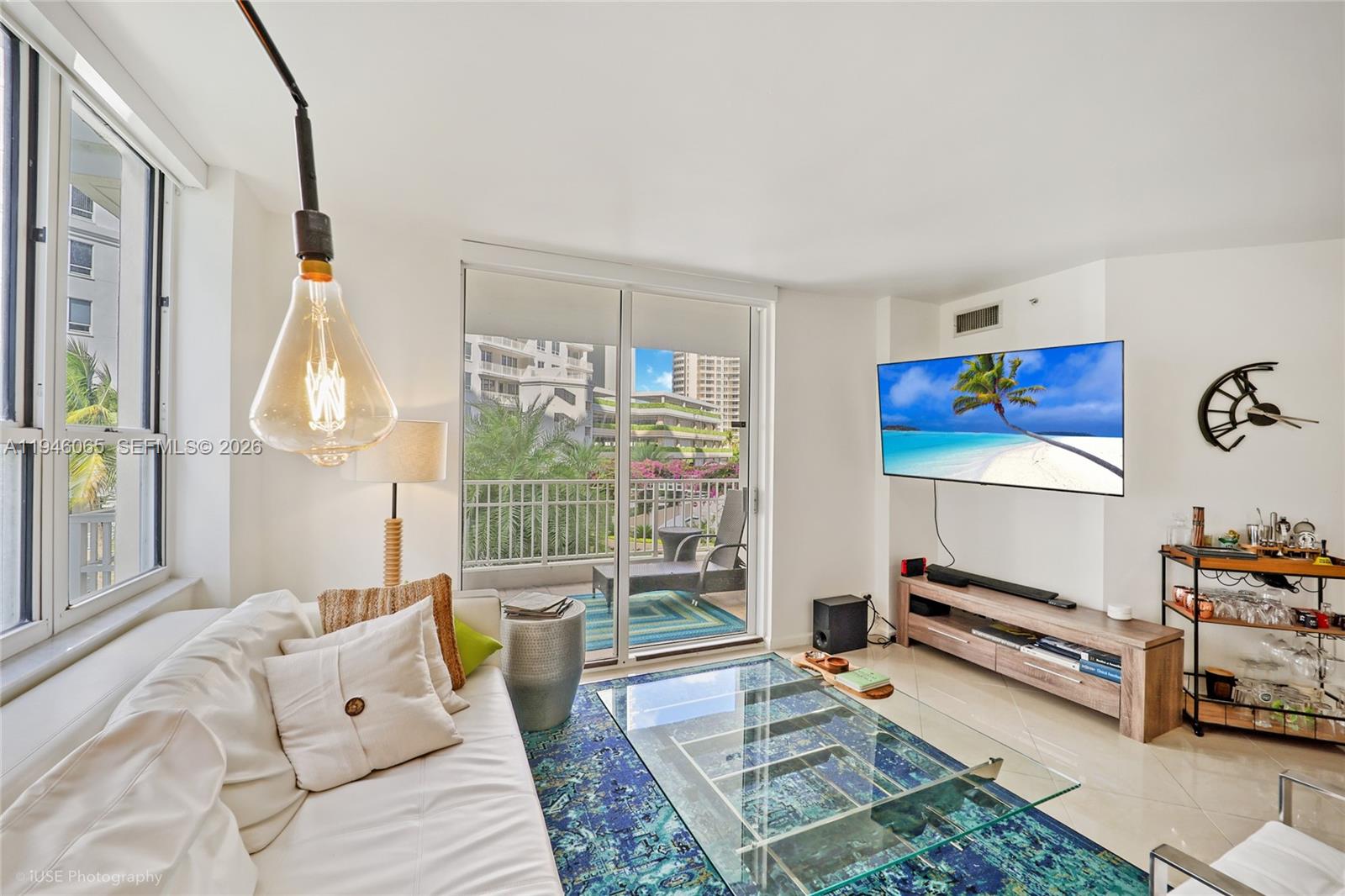 A living room features a white sofa, glass coffee table, wall-mounted television, and balcony access — 701 Brickell Key Blvd # 404, Miami FL 33131, MIAMI, FL
