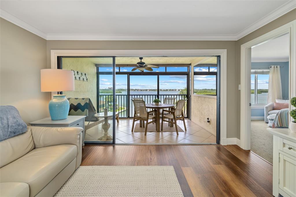A living room with wood floors opens to a screened balcony overlooking a body of water — 8911 MIDNIGHT PASS ROAD UNIT 409, SARASOTA, FL