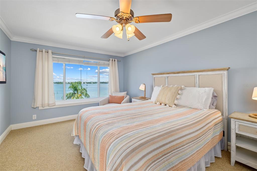 A bedroom features a bed with a striped quilt, a ceiling fan, and a water view — 8911 MIDNIGHT PASS ROAD UNIT 409, SARASOTA, FL