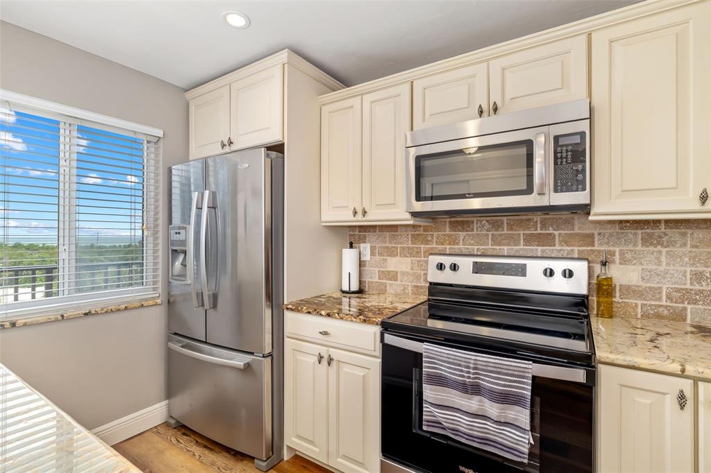 A kitchen features cream cabinets, stainless steel appliances, a brick backsplash, and a window view — 8911 MIDNIGHT PASS ROAD UNIT 409, SARASOTA, FL