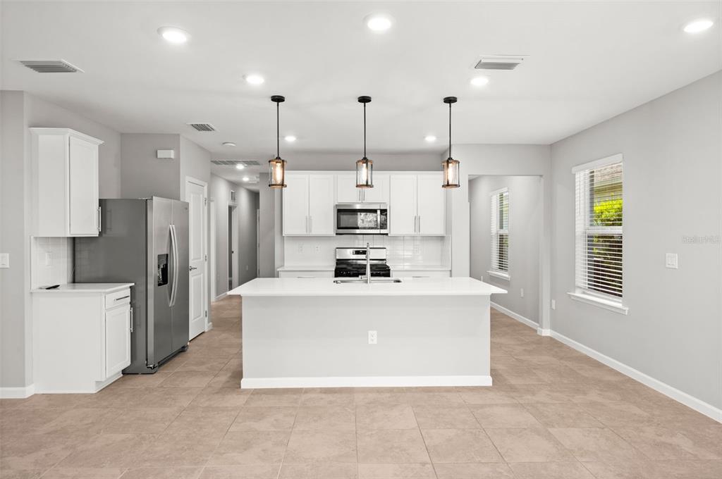 A modern kitchen features white cabinetry, stainless steel appliances, a center island, and tile flooring — 44201 KELLY DRIVE, PUNTA GORDA, FL