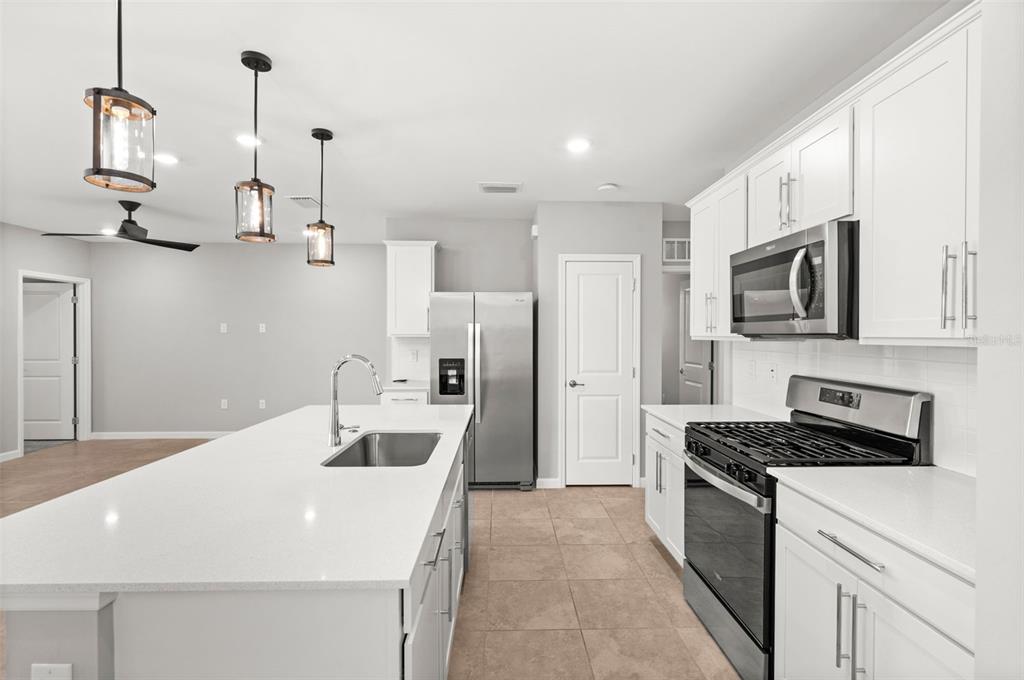 A modern kitchen features white cabinets, stainless steel appliances, a large island, and tile flooring — 44201 KELLY DRIVE, PUNTA GORDA, FL