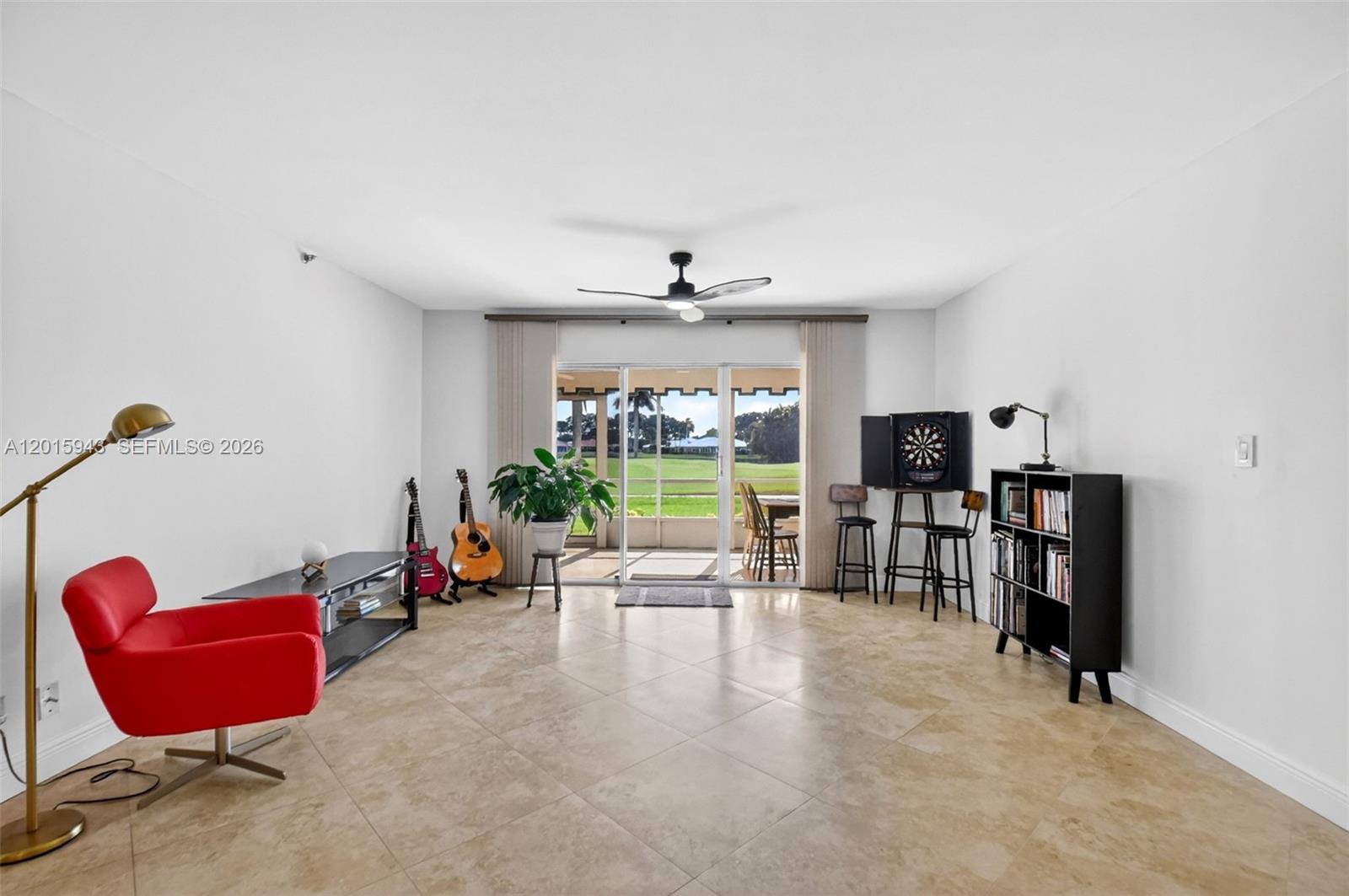 A living room features tile flooring, a red chair, musical instruments, and a sliding glass door — 300 John F Kennedy Dr # 101, Atlantis FL 33462, ATLANTIS, FL