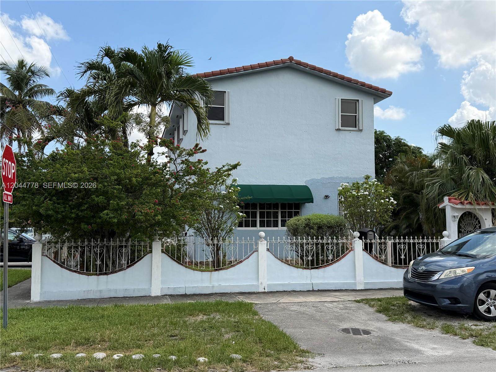 A two-story light blue house features a green awning, white decorative fence, and palm trees — 101 E 51st Pl # 0, Hialeah FL 33013, HIALEAH, FL