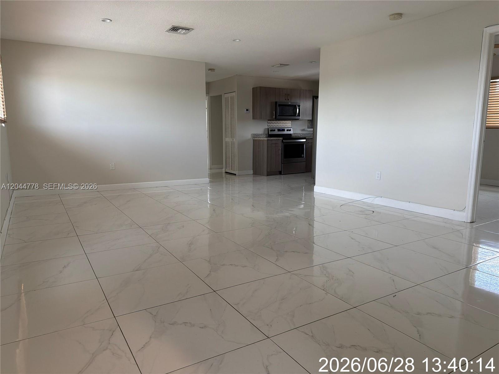 An open-concept living area features large white marble-look floor tiles and a distant kitchen — 101 E 51st Pl # 0, Hialeah FL 33013, HIALEAH, FL