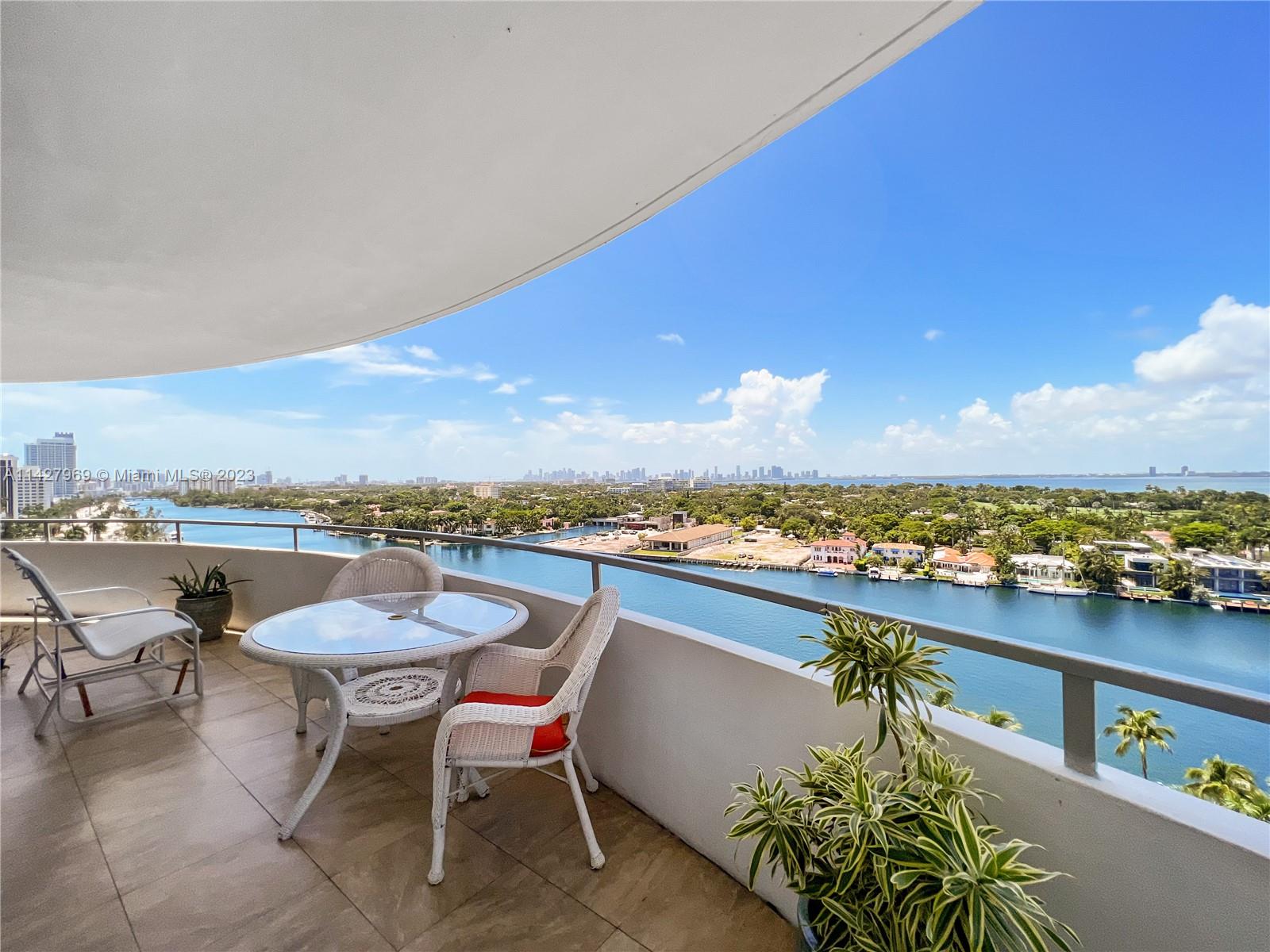 A balcony with patio furniture overlooks a waterway and a distant city skyline — 5151 Collins Ave # 1523, Miami Beach FL 33140, MIAMI BEACH, FL