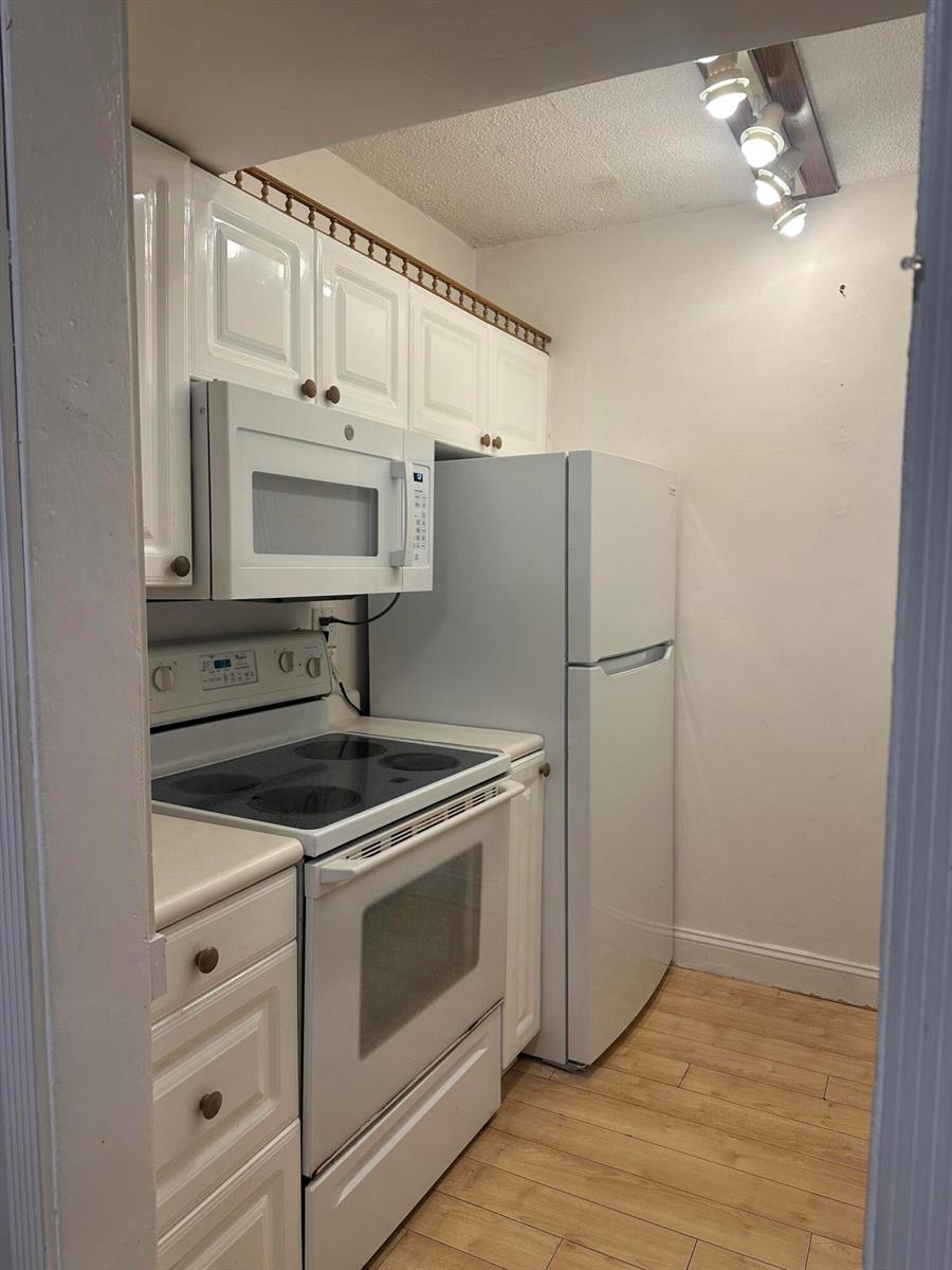 A small kitchen features white cabinets, white appliances, and light wood-look flooring — 2565 S Ocean Boulevard # C, Palm Beach FL 33480, PALM BEACH, FL