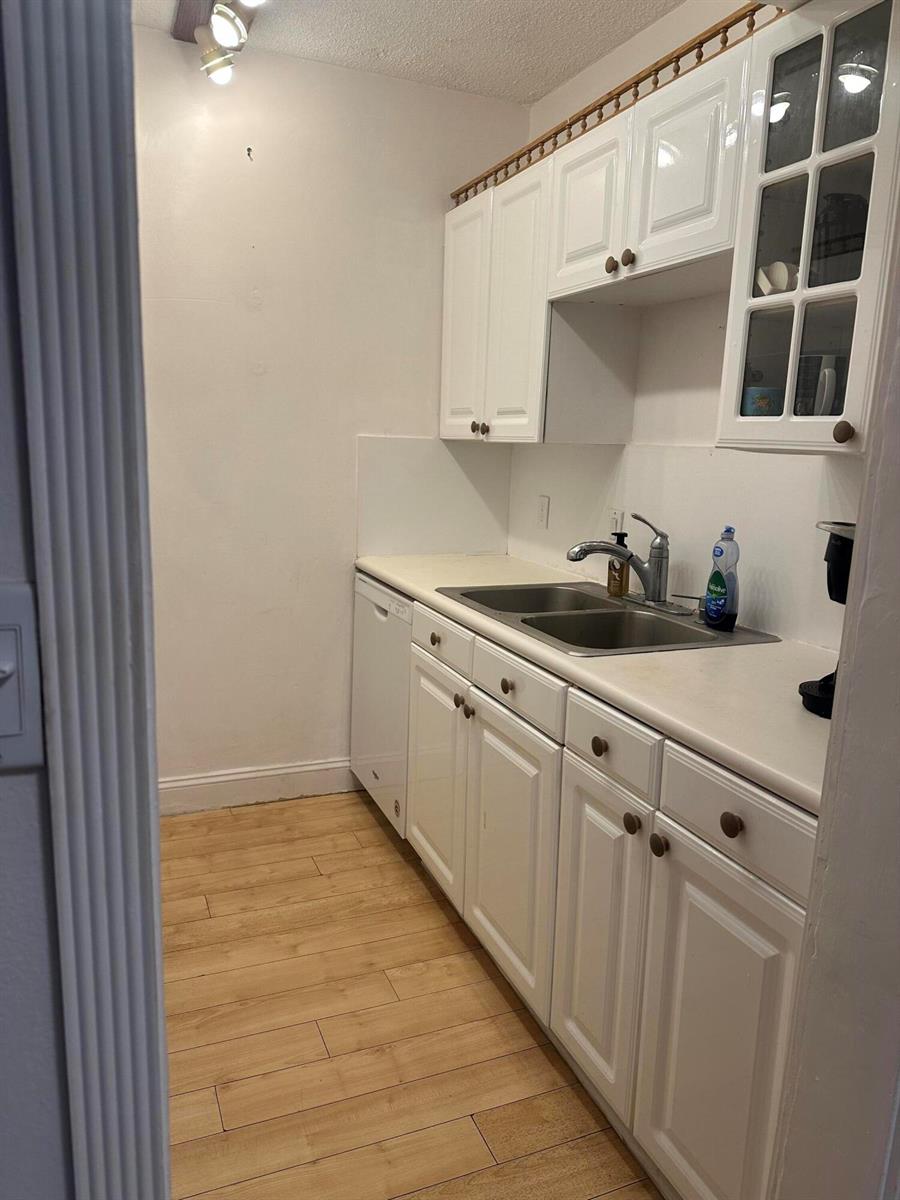 A galley-style kitchen features white cabinets, a stainless steel sink, and light wood-look flooring — 2565 S Ocean Boulevard # C, Palm Beach FL 33480, PALM BEACH, FL