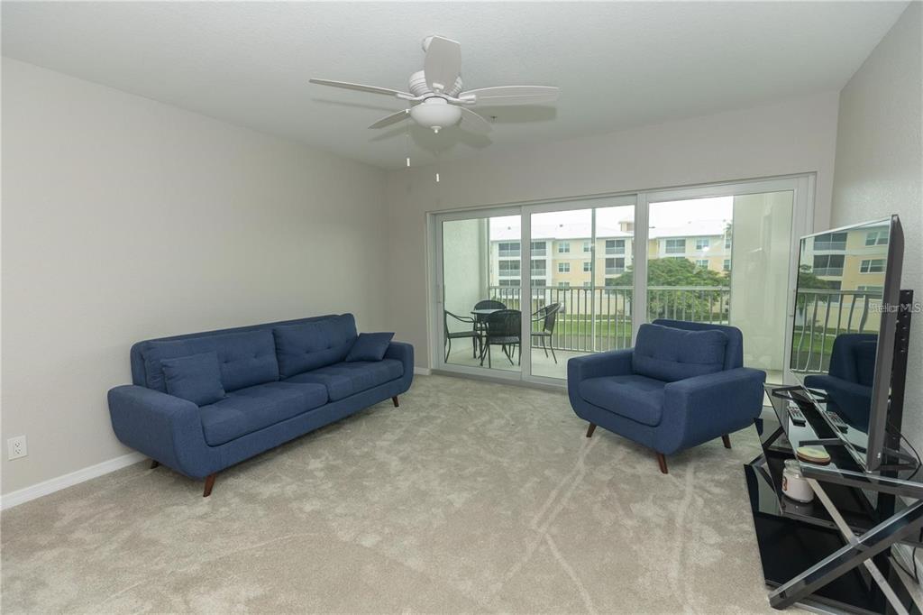 A living room features a blue sofa, matching armchair, carpeted floors, and a sliding glass door — 8403 PLACIDA ROAD UNIT 303, PLACIDA, FL