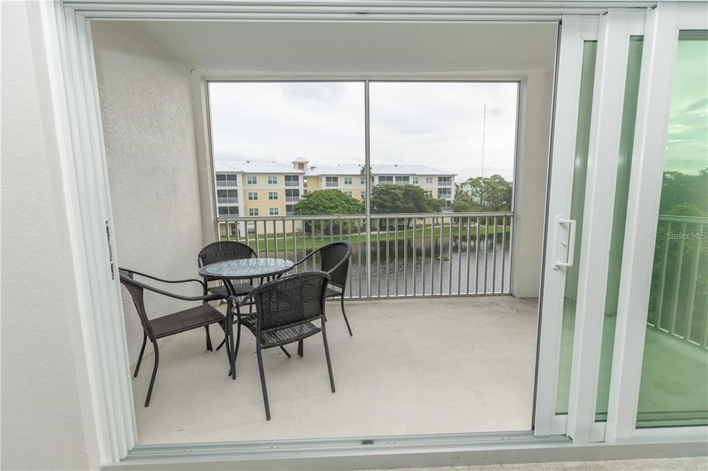 A screened-in balcony features a small table and four chairs overlooking a pond and buildings — 8403 PLACIDA ROAD UNIT 303, PLACIDA, FL