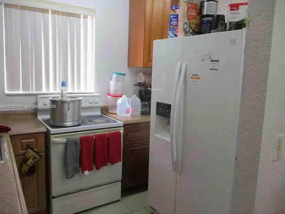 A kitchen features a white refrigerator, a white electric stove, and wood-toned cabinetry — 10040 NW 8th Ave, Miami FL 33150, MIAMI, FL