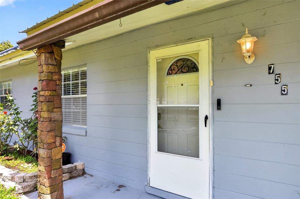 A gray house exterior features a white storm door, a stone pillar, and house numbers — 755 PARK LANE, KISSIMMEE, FL