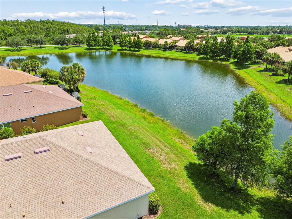 An aerial view shows suburban houses with tan roofs situated beside a large retention pond — 3420 FALLBROOK DR, KISSIMMEE, FL