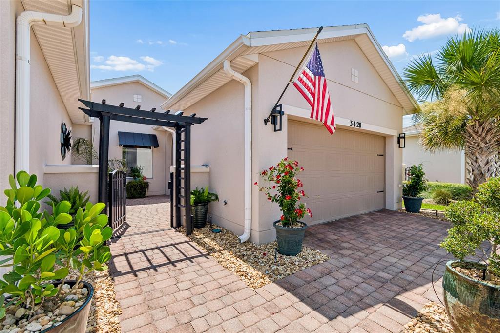 A beige house exterior features a brick driveway, a black pergola, and an American flag — 3420 FALLBROOK DR, KISSIMMEE, FL