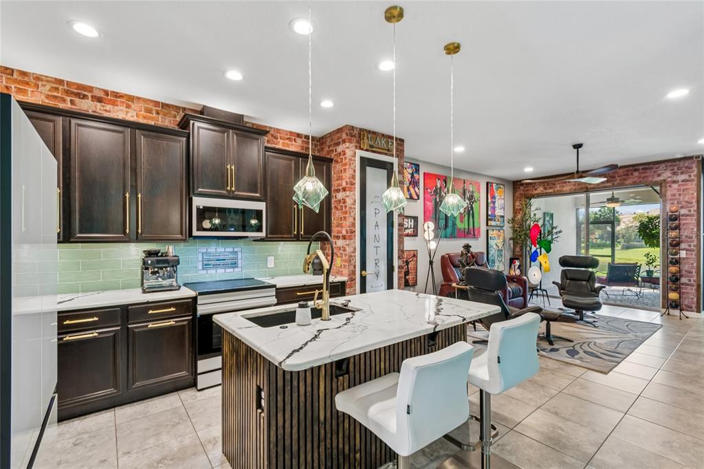 A kitchen with dark cabinets, a marble island, and brick walls opens into a living area — 3420 FALLBROOK DR, KISSIMMEE, FL