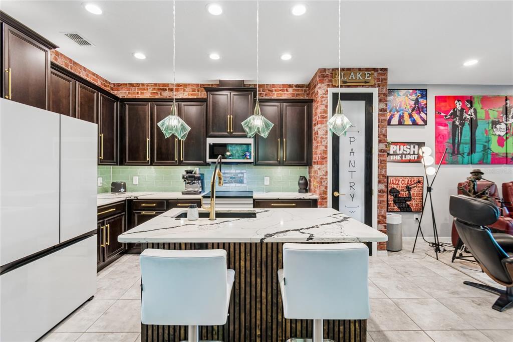A kitchen features dark wood cabinets, a marble-topped island, and an exposed brick accent wall — 3420 FALLBROOK DR, KISSIMMEE, FL