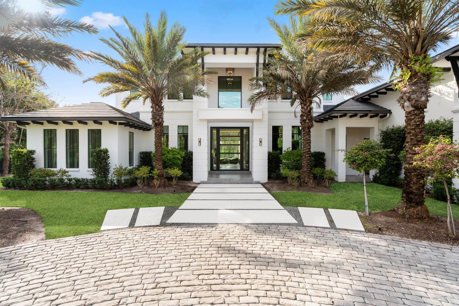 A modern white two-story house features a stone paver driveway and a central glass entryway — 210 Bears Club Drive, Jupiter FL 33477, JUPITER, FL