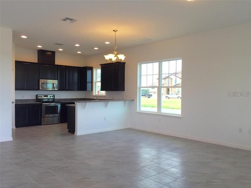 A kitchen with dark cabinets and stainless steel appliances opens to a tiled living area — 9350 WOODCRANE DRIVE, WINTER GARDEN, FL