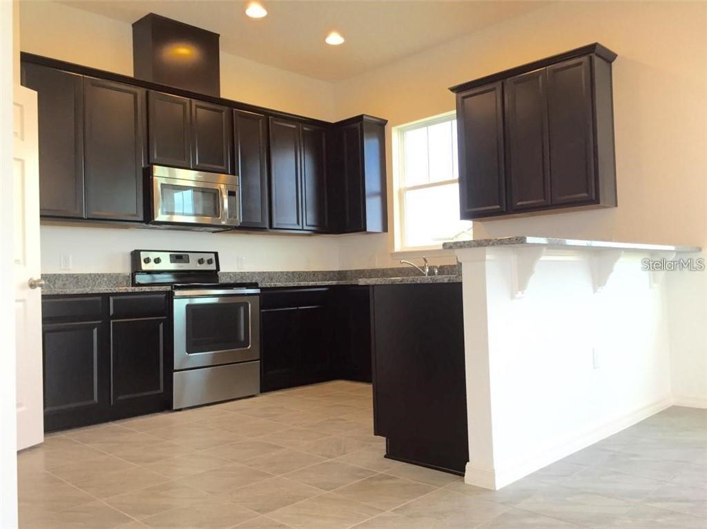 A kitchen features dark wood cabinets, stainless steel appliances, and a granite-topped breakfast bar — 9350 WOODCRANE DRIVE, WINTER GARDEN, FL
