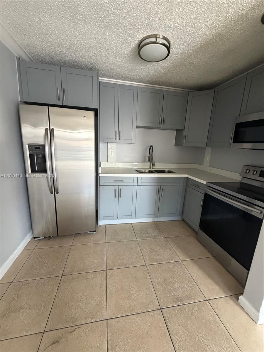 A kitchen features gray cabinets, stainless steel appliances, and beige tile flooring — 2924 NW 132nd Ter # 2, Opa-Locka FL 33054, OPA-LOCKA, FL