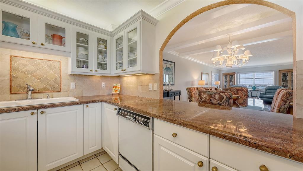 A kitchen with white cabinets and granite countertops opens into a living room with a chandelier — 9393 MIDNIGHT PASS ROAD UNIT P4, SARASOTA, FL