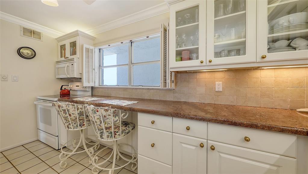 A kitchen features white cabinets, a granite countertop, two patterned chairs, and a tiled backsplash — 9393 MIDNIGHT PASS ROAD UNIT P4, SARASOTA, FL