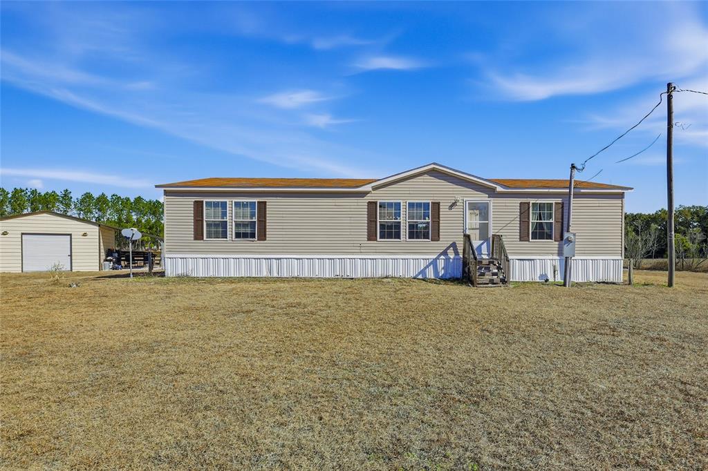 A beige manufactured home with brown shutters sits on a large, dry grass lot — 2400 NW 5TH STREET, BELL, FL