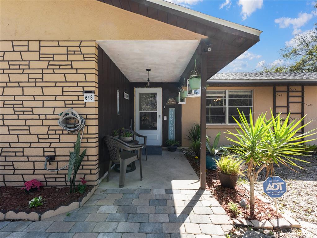 A front porch with a stone walkway, two chairs, and a brick-patterned exterior wall — 613 S WILLOW AVENUE, AVON PARK, FL