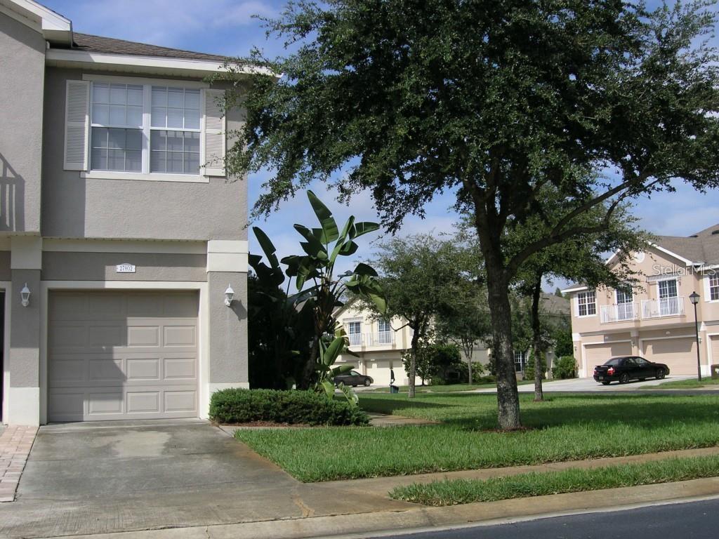 A two-story townhouse with a beige stucco exterior, a single-car garage, and a front lawn — 27802 PLEASURE RIDE LOOP, WESLEY CHAPEL, FL