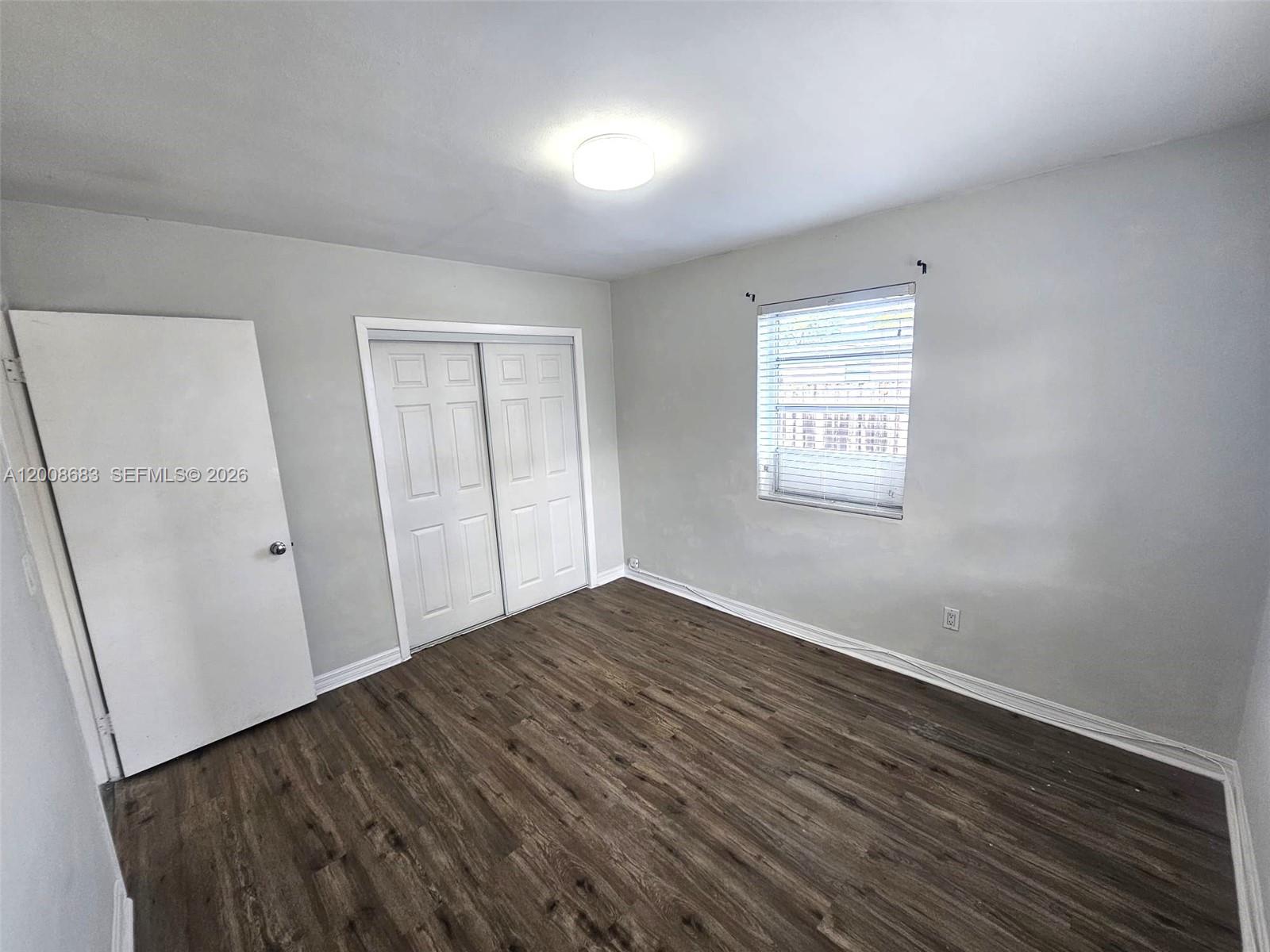 An empty bedroom features light gray walls, wood-look flooring, a window, and white closet doors — 10790 SW 46th St # 10790, Miami FL 33165, MIAMI, FL