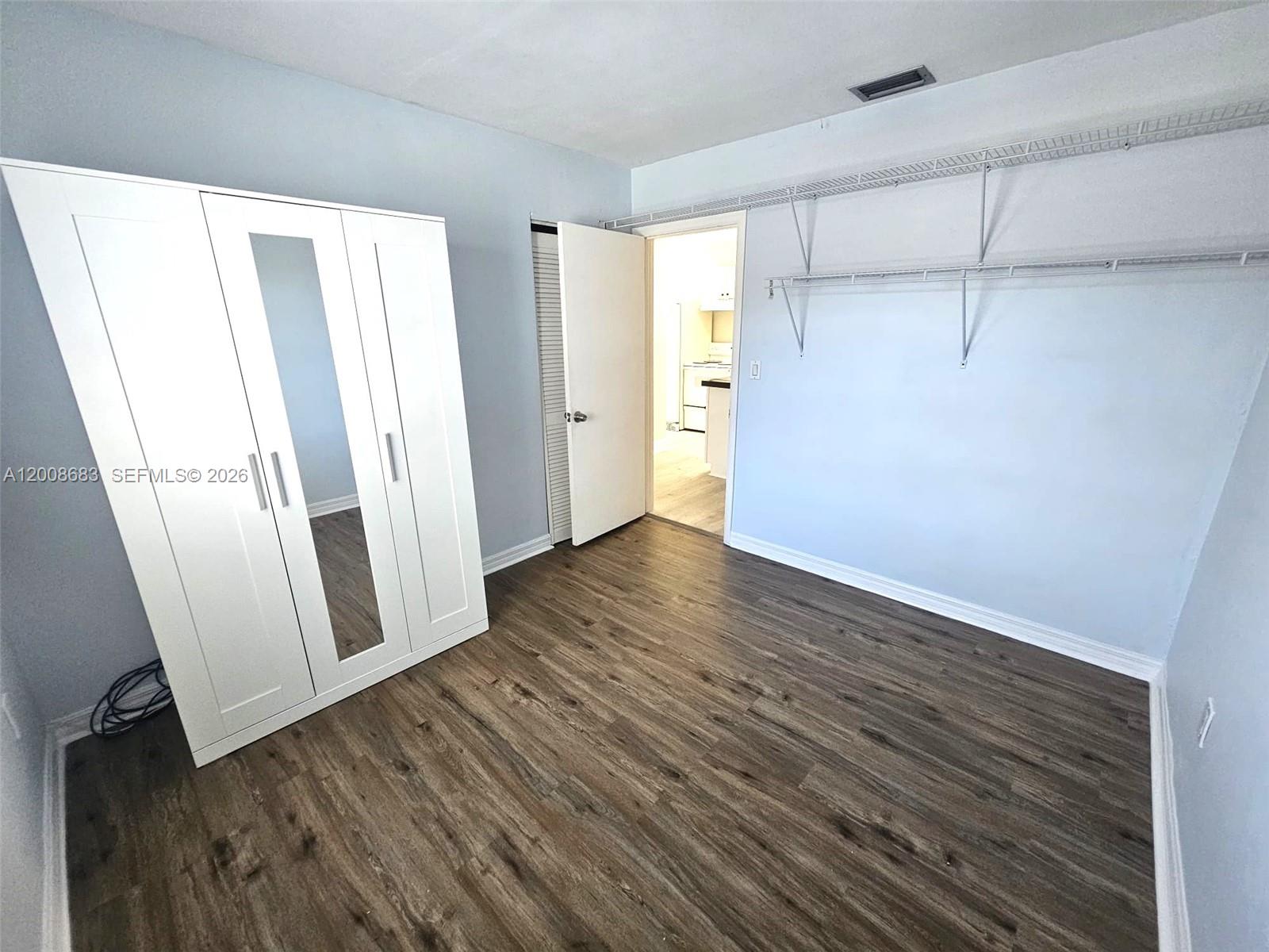 A bedroom features light blue walls, wood-look flooring, a white wardrobe, and wall-mounted shelving — 10790 SW 46th St # 10790, Miami FL 33165, MIAMI, FL