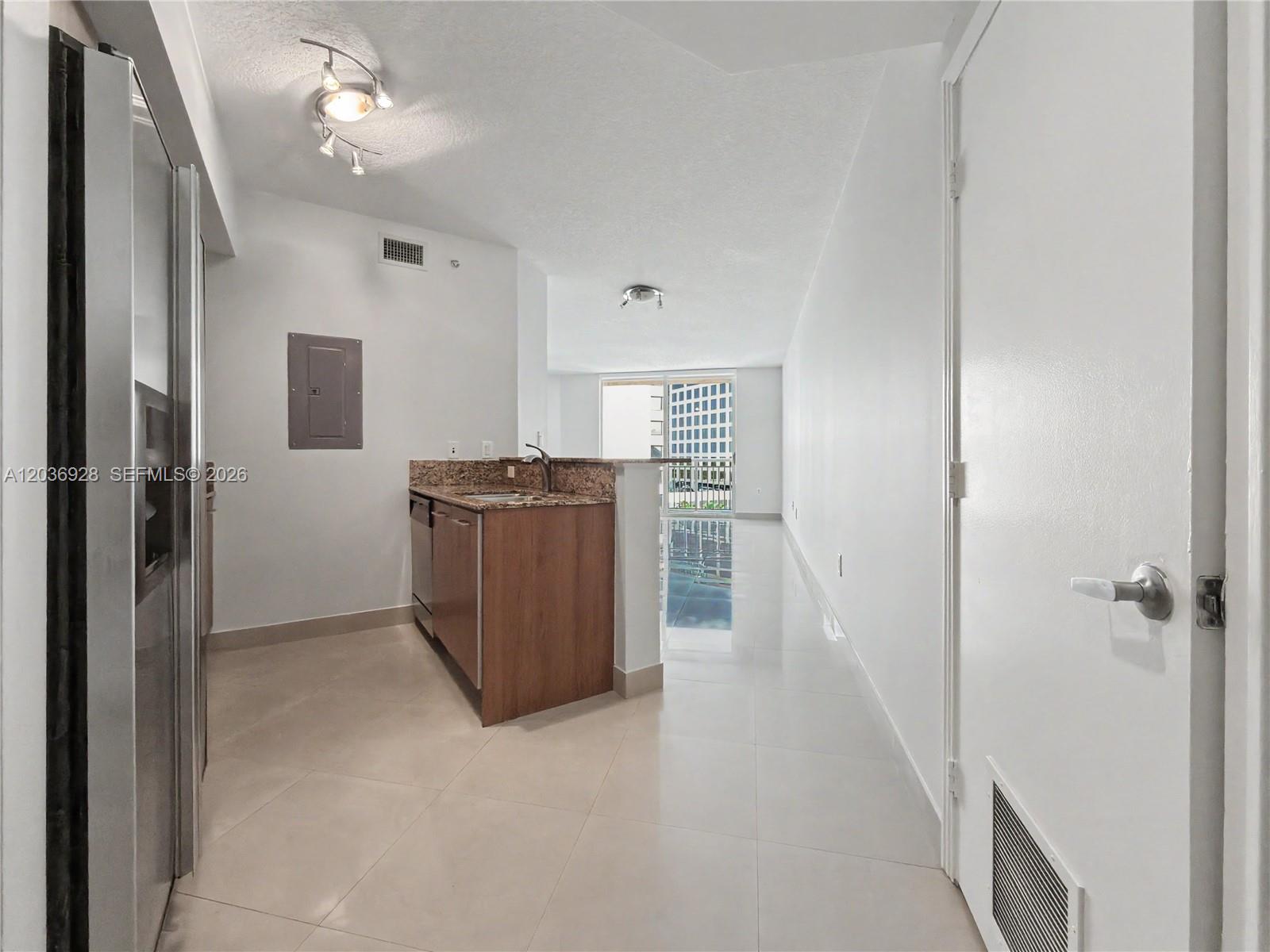 A kitchen with wood cabinets and granite countertops opens into a bright, tiled living area — 9055 SW 73rd Ct # 1004, Pinecrest FL 33156, PINECREST, FL