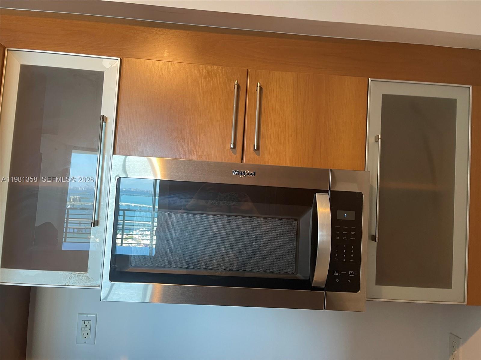 A stainless steel Whirlpool microwave is mounted between two glass-front cabinets with wood-toned doors — 335 S Biscayne Blvd # 3610, Miami FL 33131, MIAMI, FL